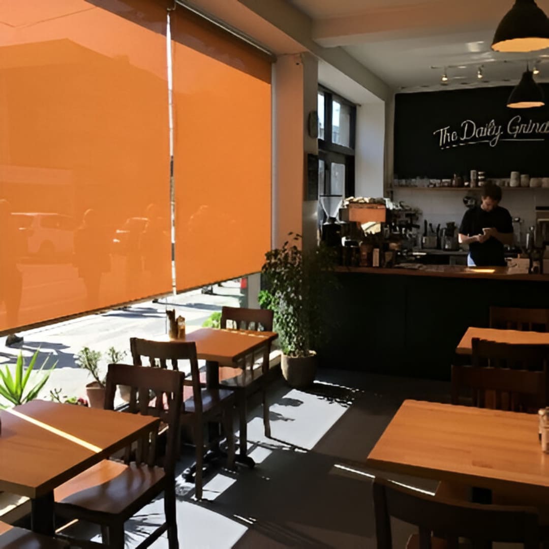 A cozy cafe with warm, amber-colored tinted PVC blinds, casting a soft light on the wooden tables and chairs.