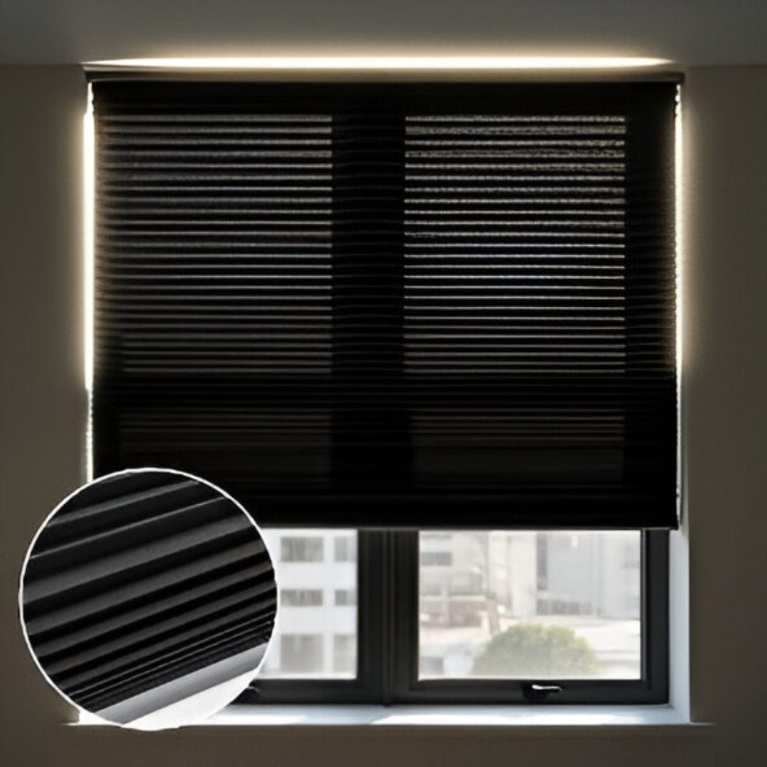 A large window covered by dark grey blackout honeycomb blinds. A soft halo of light is visible around the edges, highlighting the blinds' effectiveness at blocking light. A magnified inset shows the detailed cellular texture of the blackout fabric.