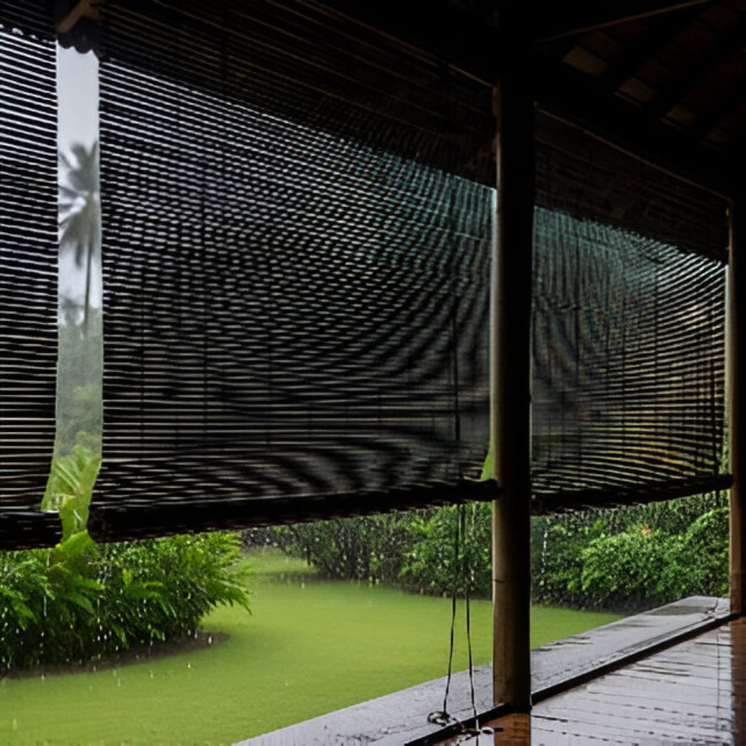 A rustic outdoor patio covered with bamboo monsoon blinds. The wet, dark slats glisten, protecting the space from rain while adding a natural, tropical aesthetic.