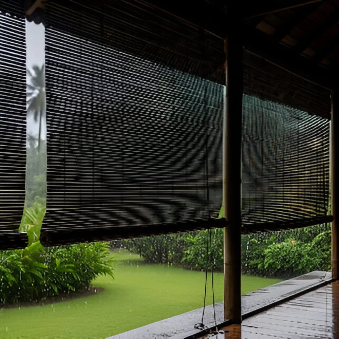 A rustic outdoor patio covered with bamboo monsoon blinds. The wet, dark slats glisten, protecting the space from rain while adding a natural, tropical aesthetic.