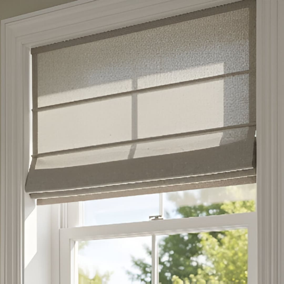 A set of modern, flat-fold Roman blinds in a light beige linen fabric, pulled halfway down over a window. The blinds have a smooth, clean appearance with crisp horizontal folds.