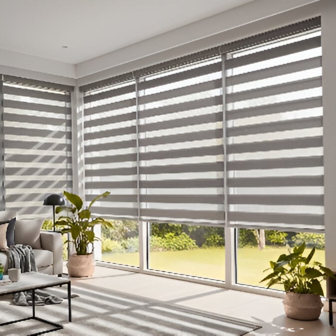 A modern living room with large windows fitted with room-darkening sheer shades. The shades are in a neutral, light grey colour, with alternating opaque and sheer horizontal fabric strips that have been lowered to darken the room.