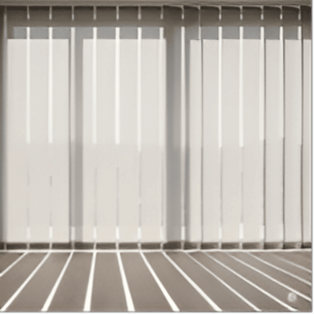 A set of elegant vertical blinds, featuring wide, off-white fabric louvres, is shown from a slightly low angle. The blinds are partially open, allowing soft, diffused sunlight to filter into a modern living room. The light creates distinct, elongated shadows on a light-wood floor. 