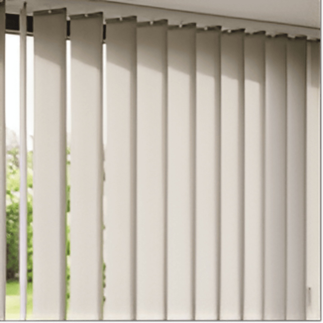 A close-up, eye-level shot of contemporary fabric vertical blinds, displaying a neutral beige colour and a subtle textured weave. The blinds are partially open, with some individual fabric slats rotated to allow soft, diffused light to filter through a large window. 