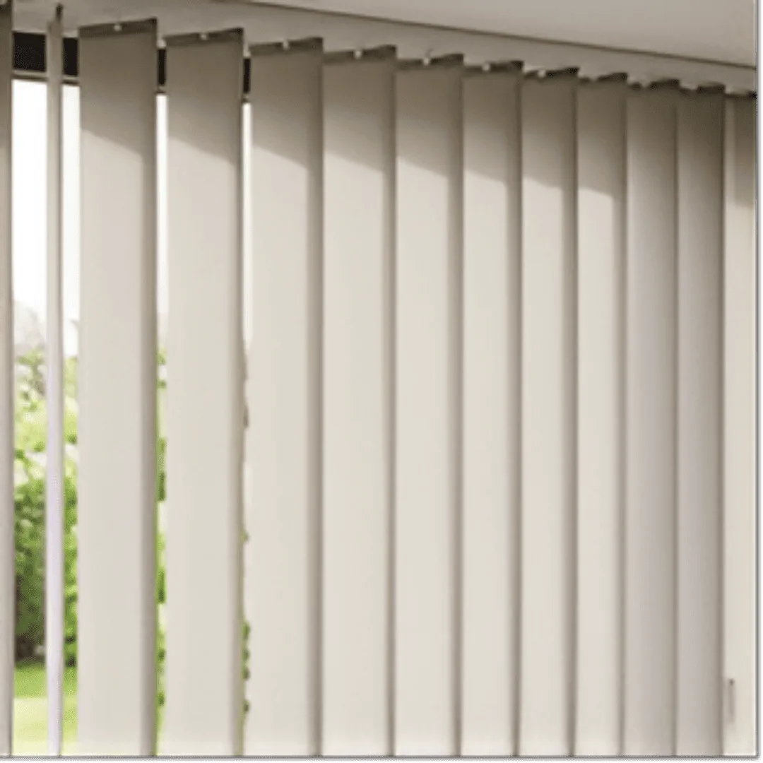 A close-up, eye-level shot of contemporary fabric vertical blinds, displaying a neutral beige colour and a subtle textured weave. The blinds are partially open, with some individual fabric slats rotated to allow soft, diffused light to filter through a large window. 