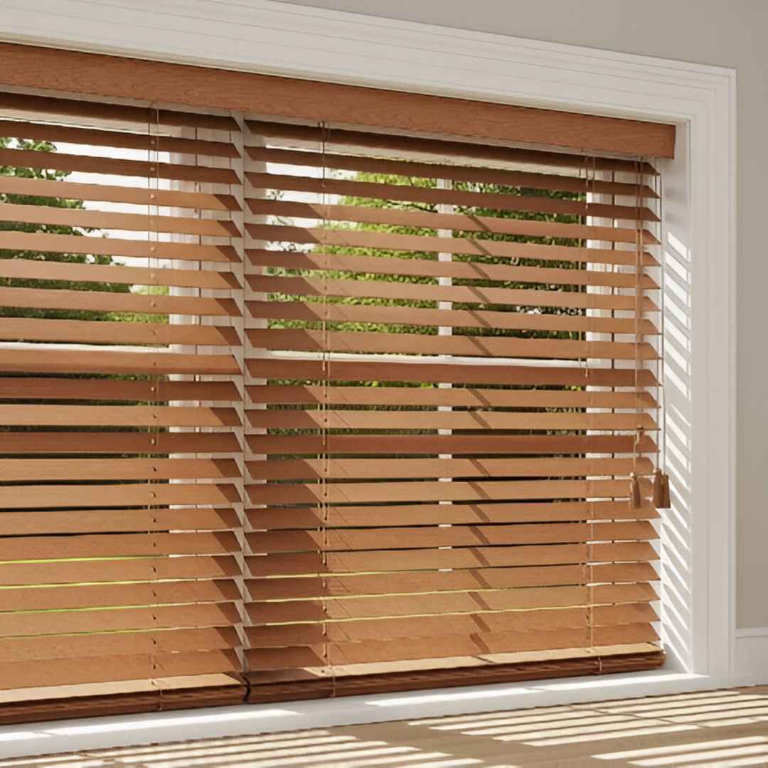 A window with faux wood blinds in a medium oak finish. The blinds are tilted slightly open, showing off the wood-like grain and allowing light to enter the room.