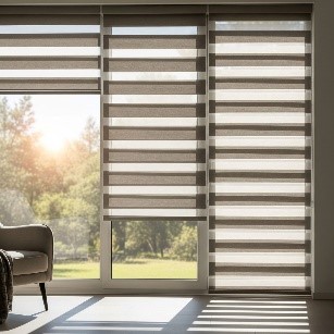 A sunlit living room with light-filtering zebra blinds on a large window. The blinds have alternating sheer and solid stripes in a neutral beige colour, allowing soft, diffused light to enter the room.