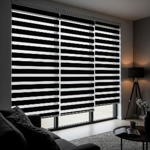 A dimly lit living room with blackout zebra blinds on a window. The blinds are fully closed, with opaque black and white stripes overlapping to block out all light completely.