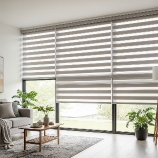 A bright living room with large windows covered in cordless zebra blinds. The blinds are a light grey and white striped pattern, providing a clean, modern look without any visible cords or chains.